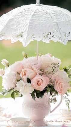 a vase with flowers and an umbrella in it on a white table cloth next to a tea cup