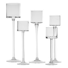 four clear glass candlesticks are lined up on a white background with one candle in the middle