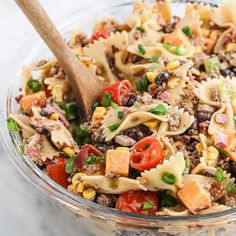 a glass bowl filled with pasta salad and a wooden spoon