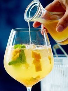 a person is pouring some liquid into a glass filled with fruit and ice cubes