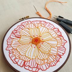 an embroidery project with scissors and thread on the table next to it is a flower