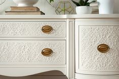 an ornate white dresser with gold handles and knobs on it's drawers, next to a potted plant