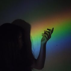 a woman holding her hand up in front of a rainbow colored wall with light coming through it