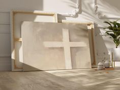 a cross is on the floor next to two framed pictures and a potted plant