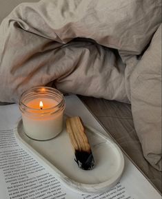 an open book with a lit candle on it next to a glass jar filled with matches