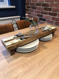 a wooden table topped with plates and vase filled with flowers next to a brick wall