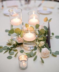 candles are lit on the table with flowers and greenery