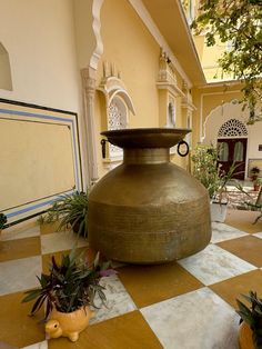 a large metal vase sitting on top of a checkered floor next to potted plants