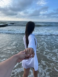 two people holding hands while walking into the water at the beach on a cloudy day