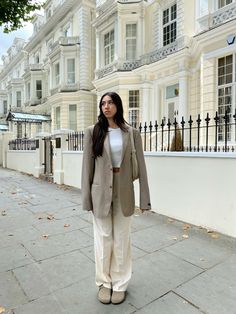 a woman is standing on the sidewalk in front of some white buildings and trees with her hands in her pockets