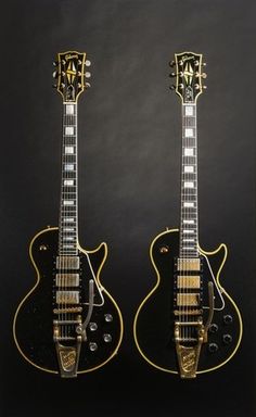 two guitars are sitting side by side on a black background, one is gold and the other is black