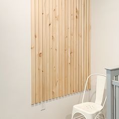 a white chair sitting next to a baby crib in a room with wooden slats on the wall