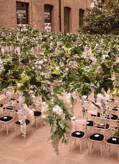 an outdoor wedding venue with chairs and flowers on the aisle, in front of a brick building