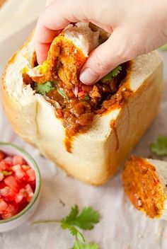 a person is dipping some food into a breaded roll with meat and vegetables on the side