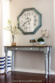 a clock on the wall above a table with vases and flowers in front of it