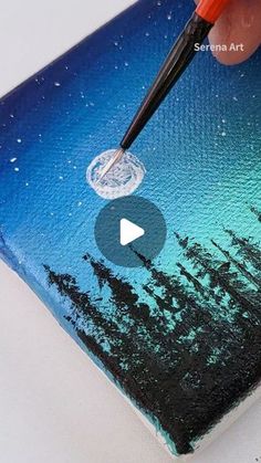 someone is using a brush to paint the sky and trees on a piece of paper