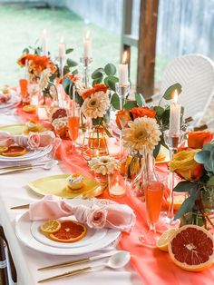 the table is set with oranges, flowers and candles for an elegant dinner party