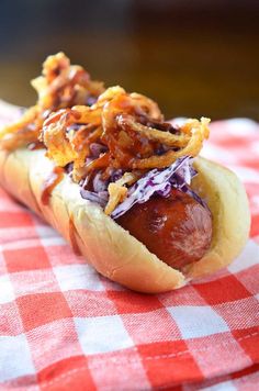 a hot dog with onions and ketchup sitting on a red and white checkered table cloth