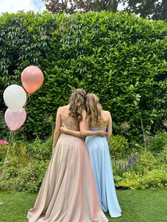 two women in long dresses standing next to each other with balloons and bushes behind them