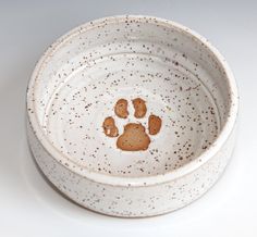 a white bowl with brown speckles and a dog's paw on it