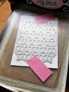 some pink and white pieces of paper sitting on top of a cutting board next to a machine