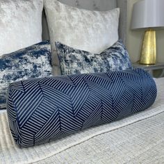 a bed with blue and white pillows on top of it's headboard, next to a lamp