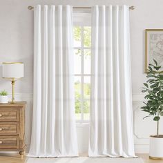 a white curtain hanging in front of a window with a potted plant next to it