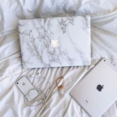 an apple laptop computer sitting on top of a bed next to headphones and ear buds