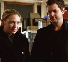 a man and woman standing next to each other in front of a bookshelf