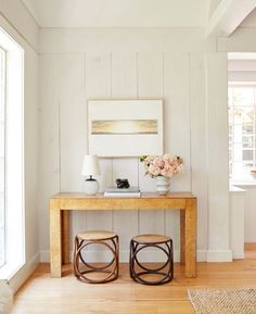 a wooden table with two stools in front of it next to a painting on the wall