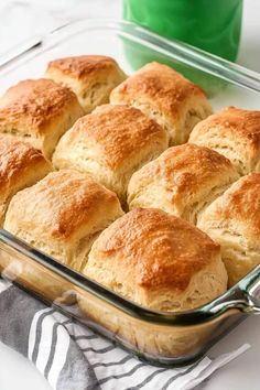 a casserole dish filled with freshly baked biscuits and sitting on a towel next to a green cup