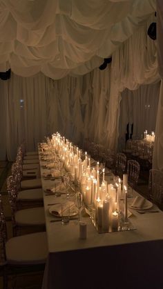 a long table with many lit candles on it in front of white draping