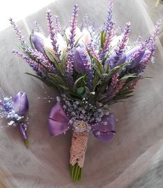 a bouquet of purple flowers sitting on top of a white cloth covered table next to a boutonniere