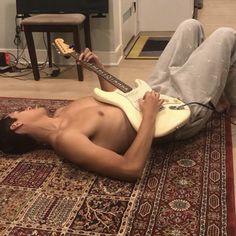 a shirtless man laying on the floor with an electric guitar strapped to his neck