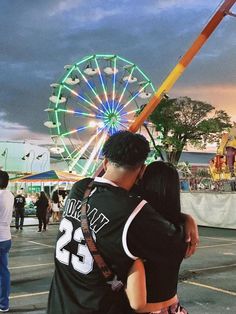 a man and woman hugging in front of a ferris wheel