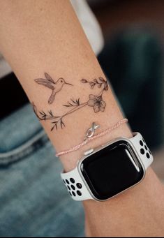 a woman's arm with a bird and flower tattoo on it, while she is wearing a white apple watch