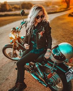 a woman sitting on top of a motorcycle in the middle of a dirt road with grass and trees behind her