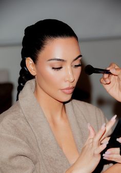 a woman is getting her make - up done with a brush and eyeliner pencil