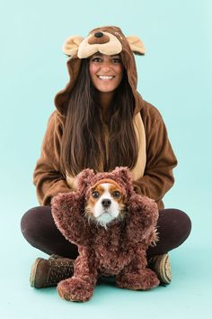 a woman is holding a small dog wearing a bear costume on her head and sitting in front of a blue background