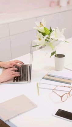 a woman is typing on her laptop while sitting at a desk with flowers in the background