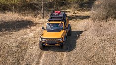 a yellow truck driving down a dirt road in the middle of some brush and trees