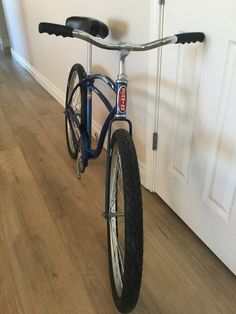 a blue bike parked in front of a door on a wooden floor next to a white wall