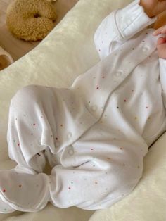 a baby laying on top of a bed next to a teddy bear