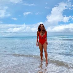 a woman in a red swimsuit is walking into the water at the edge of the beach