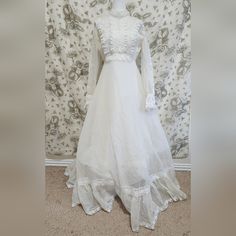 a white wedding dress is displayed on a mannequin head stand in front of a floral wallpaper