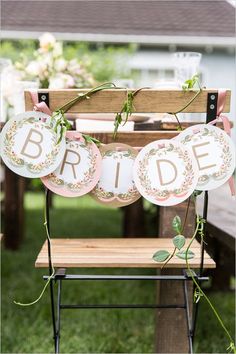 the bride and groom's plates are hanging from a wooden bench in front of an outdoor table