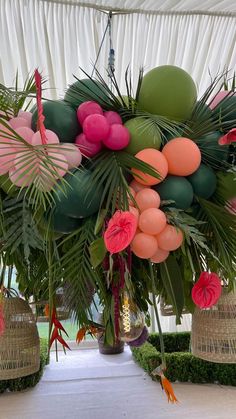 an arrangement of palm leaves, balloons and flowers on display in a tented area