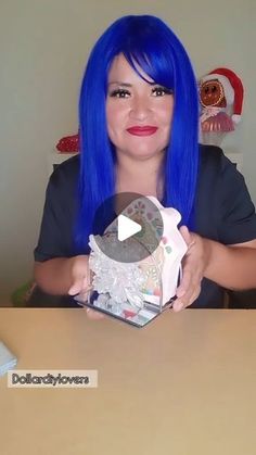 a woman with blue hair sitting at a table in front of a computer screen and holding a box