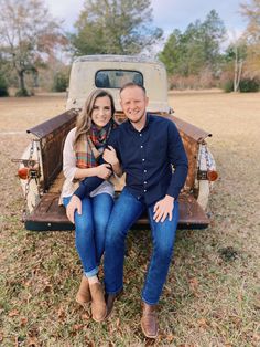 a man and woman sitting on the back of an old pickup truck in a field