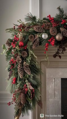 a christmas wreath with pine cones, berries and evergreens hanging from the mantel